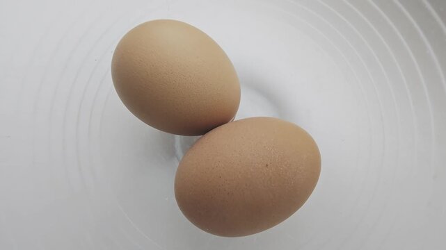 Top down view of two brown eggs spinning inside a transparent glass bowl. Healthy eating, breakfast preparation, and cooking concept