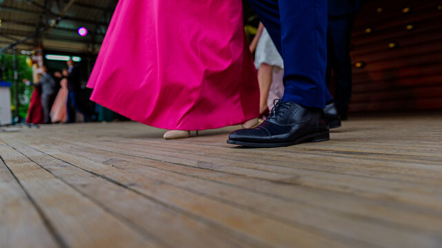 Fragment of a womans pink dress and mens shoes on a wooden floor during a dance.