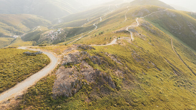Aerial view of winding dirt roads snaking along the rugged mountain ridges under a soft hazy light near the village of Aldeia das Dez, Coimbra, Portugal.