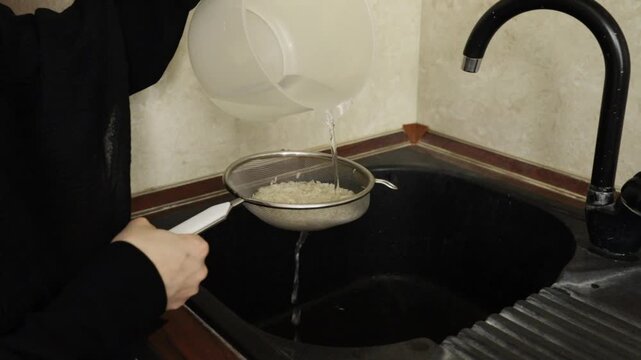 clear water is poured over uncooked basmati rice resting in a mesh strainer above the sink, highlighting an essential washing step before cooking a fragrant rice dish
