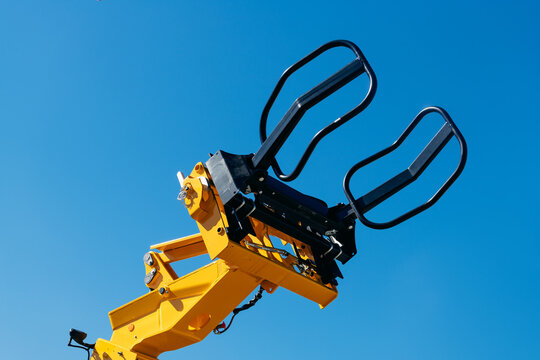 Yellow telehandler arm fitted with a black grapple attachment against a clear blue sky, highlighting heavy construction machinery hydraulic components