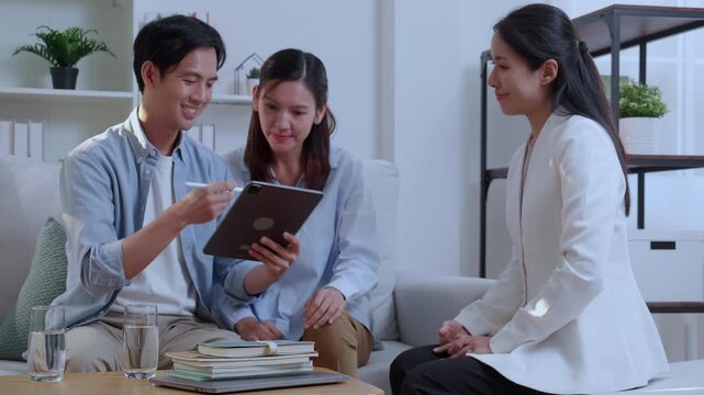 Asian couple signing digital contract on tablet screen during meeting, happy husband and wife signing electronic signature on tablet, clients approving digital insurance contract or investment.