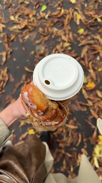 Walking in city park during golden autumn with hot drink in paper cup and fresh croissant. Woman romanticizing and enjoying fall season top view