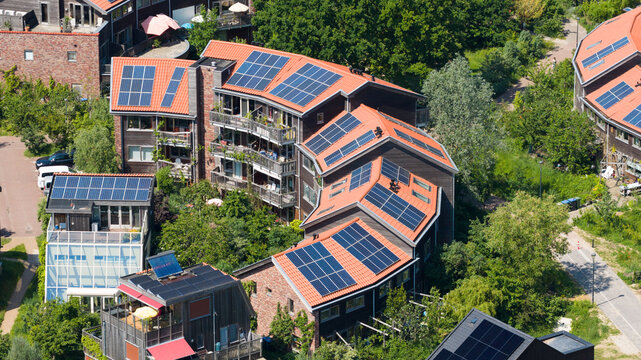 Aerial view of the Iewan sustainable housing project featuring solar panels on red-tiled roofs and wooden facades surrounded by lush greenery in Nijmegen, Gelderland, Netherlands.