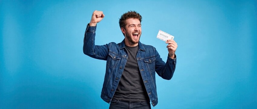Excited young man celebrating big win holding ticket on blue background