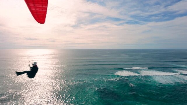 Drone shot of a man paragliding above the ocean, water
