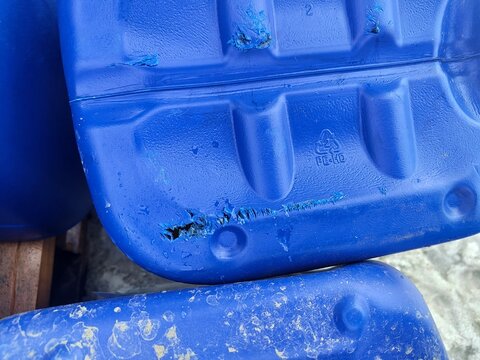 close up of a damaged blue plastic canister with scratches and a bite mark hole showing high density polyethylene pe