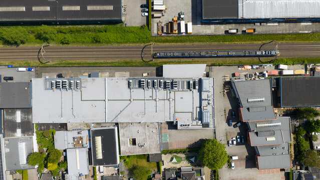 Aerial view of Eurofiber Datacenter Utrecht with HVAC units on the roof and a blue train passing on the adjacent tracks in Groenekan, Utrecht, Netherlands.