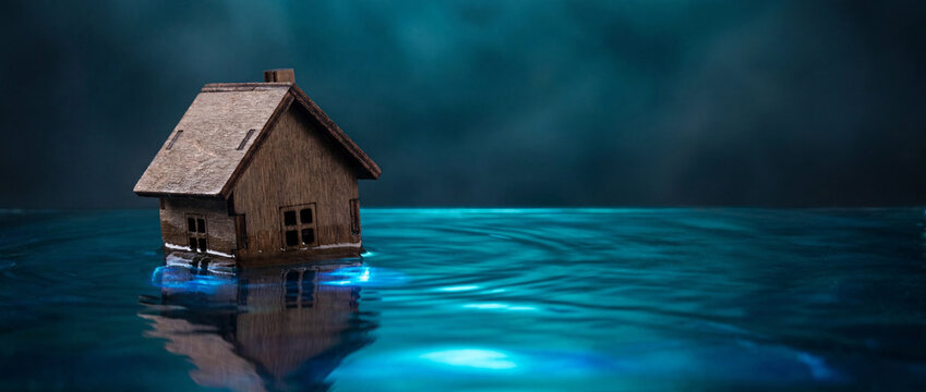 Miniature house surrounded by rising blue water flood concept