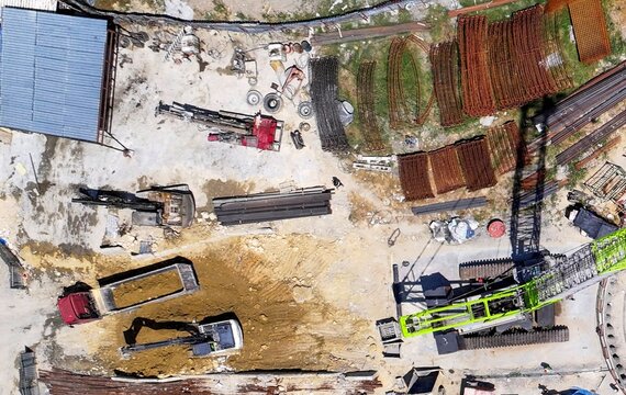 Aerial view of a busy construction site with excavators, a dump truck, and a large green crane among stacks of rebar in Avcilar, Istanbul, Turkiye.