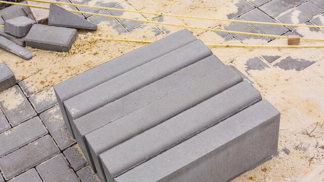 A row of grey concrete border stones stands on a sandy construction site during a walkway paving process