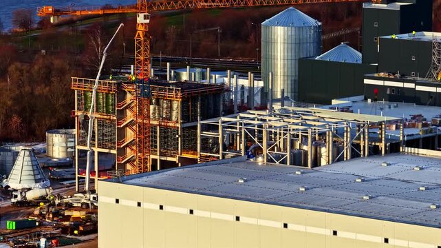 Factory complex under construction with cranes and machinery idle as the shift has finished for the day, cinematic aerial view