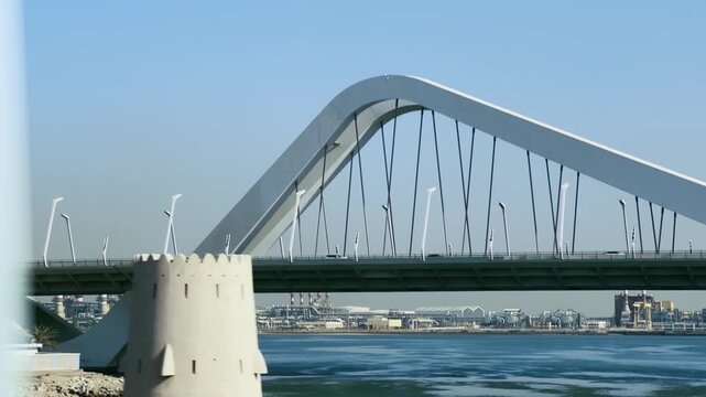 Drive along modern arch bridge with traffic spanning the water with a cityscape in Abu Dhabi