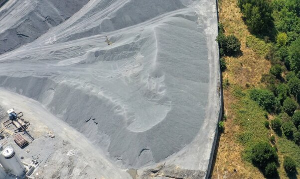 Aerial view of large piles of crushed grey stone and gravel at an industrial quarry site next to a lush green forest area Avcilar, Istanbul, Turkiye.