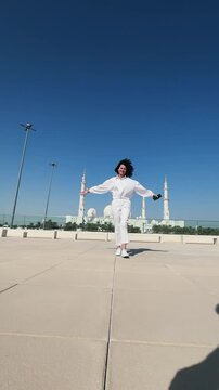 Cheerful tourist stylish woman dressed in white walk with outstretched arms near Sheikh Zayed Mosque in Abu Dhabi, United Arab Emirates, concept of victory and success, vertical video