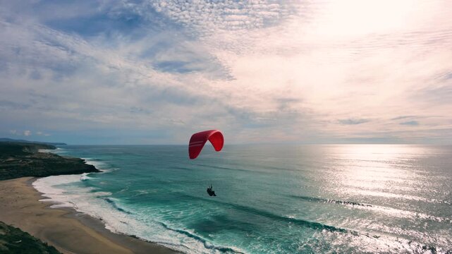 Drone shot of a man paragliding above the ocean, water