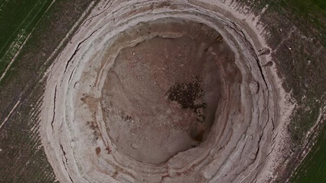 Top down drone footage inside a large dry sinkhole, showing steep eroded walls, cracked soil layers, geological textures, natural ground collapse, and karst terrain from above.