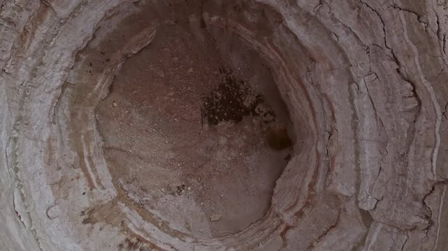 Top down drone footage inside a large dry sinkhole, showing steep eroded walls, cracked soil layers, geological textures, natural ground collapse, and karst terrain from above.