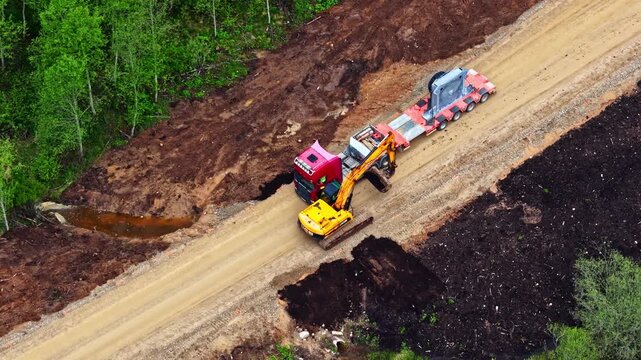 Aerial view of a large excavator clearing and grading a muddy dirt road for a semi-truck