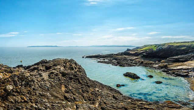 Beautiful summer coastal view from Portrane looking toward Howth Head and the Sugar Loaf mountain through rugged rock formations, Dublin, Ireland.