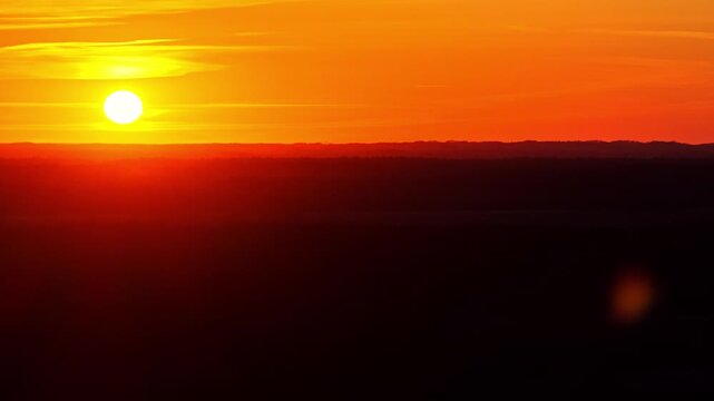 Bright sun descending behind a silhouetted landscape under a beautiful fiery orange sky