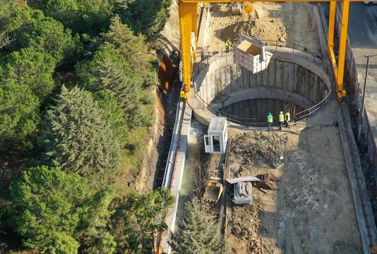 Aerial view of a large circular construction shaft with a yellow gantry crane and workers on site next to a lush green forest Avcilar, Istanbul, Turkiye.