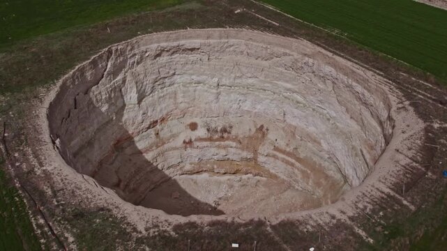 Top down drone footage showing green agricultural fields and the edge of a large sinkhole. Rural farmland, natural ground collapse, karst terrain, and landscape textures captured from above.