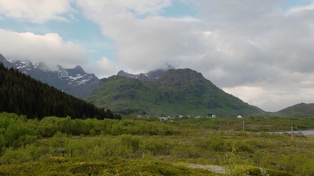 A panoramic view of a beautiful Arctic landscape in May; houses scattered around a lake surrounded by mountains on a cloudy day near Leknes, a town in the middle of the Lofoten Islands, Norway.