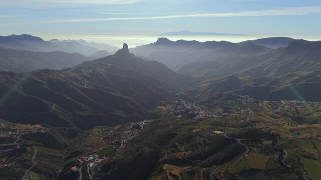 Epic aerial scenery of Roque Bentayga and a village in the Tejeda valley, with the misty silhouette of Mount Teide in the background