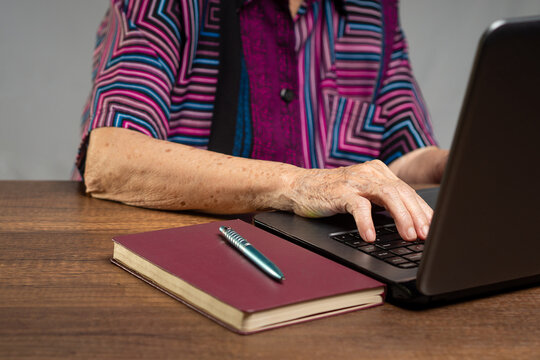 Senior Woman Using Laptop at Desk with Notebook