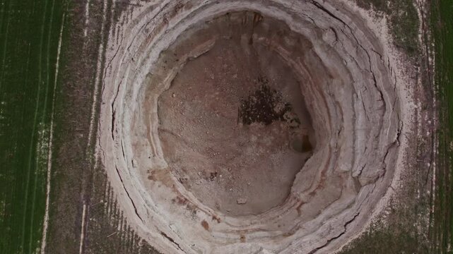 Top down drone footage inside a large dry sinkhole, showing steep eroded walls, cracked soil layers, geological textures, natural ground collapse, and karst terrain from above.