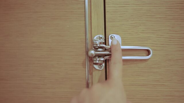 Female hand interacting locking secured metal clasp on a wooden entrance door