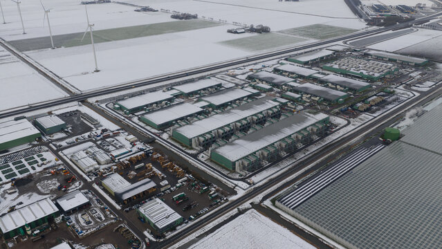 Aerial view of a large industrial complex and data center surrounded by snow-covered fields and wind turbines Middenmeer, North Holland, Netherlands.