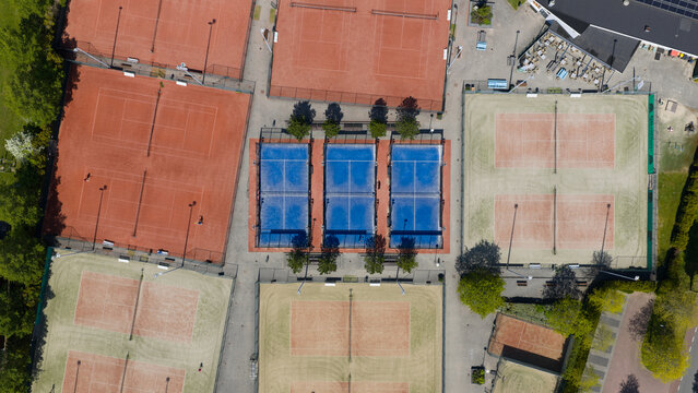 Aerial view of a sports complex featuring red clay tennis courts and blue padel courts with people playing and relaxing in Heiloo, North Holland, Netherlands.