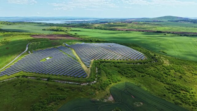 Aerial butterfly solar farm across fields, rows of tilted panels arranged in wing pattern over gentle hills, farmland and hedgerows framing site, habitat