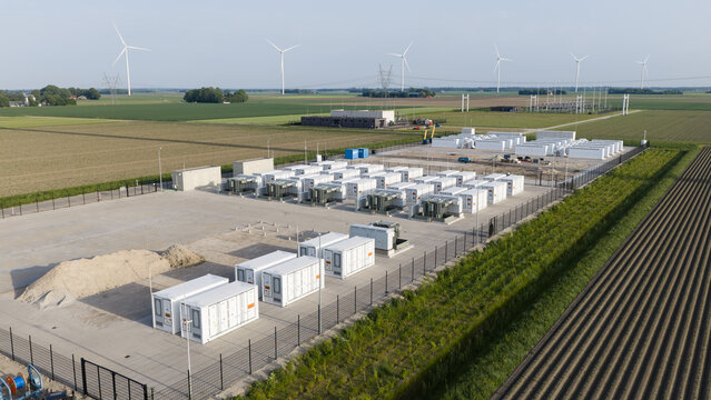 Aerial view of a battery energy storage system facility with white container units and wind turbines across agricultural fields Dronten, Flevoland, Netherlands.