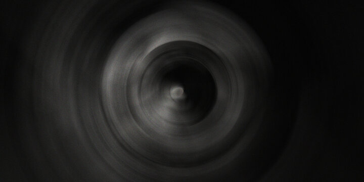 Dark monochromatic circular vortex pattern with radial motion blur effect creating depth and mystery in minimalist black tones.