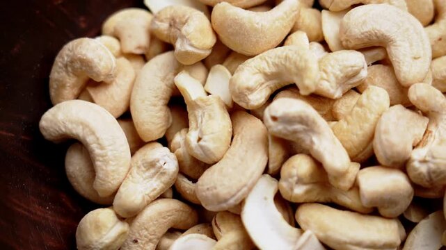 Heap of raw peeled cashew nuts in a dark wooden bowl. Nutritious organic kernels. Keto diet ingredient. Rotation