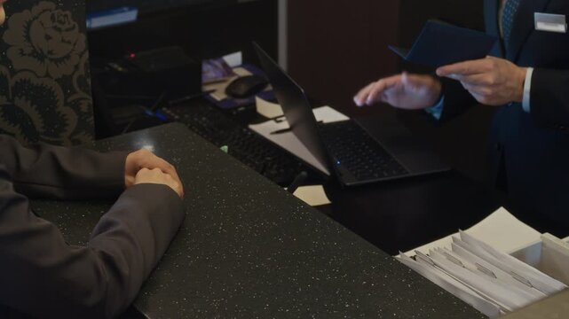 Woman handing passport to male hotel receptionist at check in desk, receiving room key card after registration. Ideal for hospitality industry, travel booking, and business trip concepts, Close Up