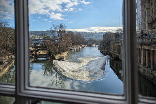 View of Pulteney Weir and River Avon through a Scenic view framed by a window looking out over the historic Pulteney Weir on the River Avon in Bath, United Kingdom. The flowing water creates a horsesh