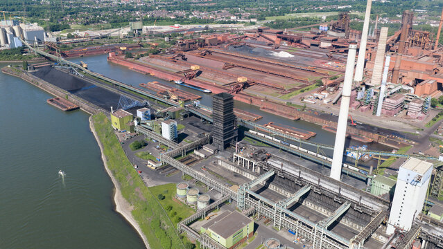 Aerial view of the Kokerei Schwelgern KBS thyssenkrupp Steel plant with industrial chimneys and coal storage facilities along the river in Duisburg, North Rhine-Westphalia, Germany.