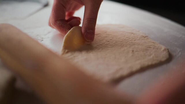 Close-up of hands rolling dough with wooden roller on floured surface. Hands move gently, ensuring even thickness. Soft focus highlights texture and motion. Ideal for recipes, baking tutorials