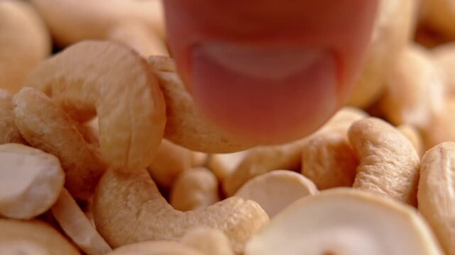 Fingers picking up a single whole cashew nut from a pile. Healthy diet concept. Organic snacking product