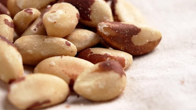 Brazil nuts scattered on natural linen fabric in close up view. Crunchy nutrient rich snack. Healthy dried ingredient. Rotation