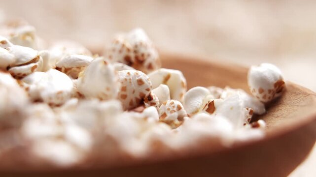 White crunchy puffed buckwheat grains falling into a rustic wooden spoon in slow motion. Fitness nutrition concept
