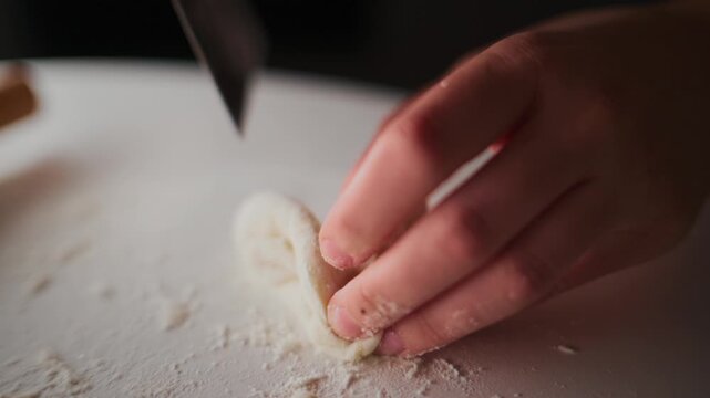 Close-up of hands shaping dough on a floured surface. Fingers gently fold and twist the dough into a decorative form. Warm lighting highlights texture and care in movement. Ideal for food blogs