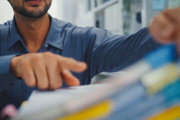 Fototapeta premium Closeup overworked young Latin businessman reading document in large stack of paperwork file at office desk. Tax audit deadline, accounting stress, corporate burnout, bookkeeping, bureaucracy concept.