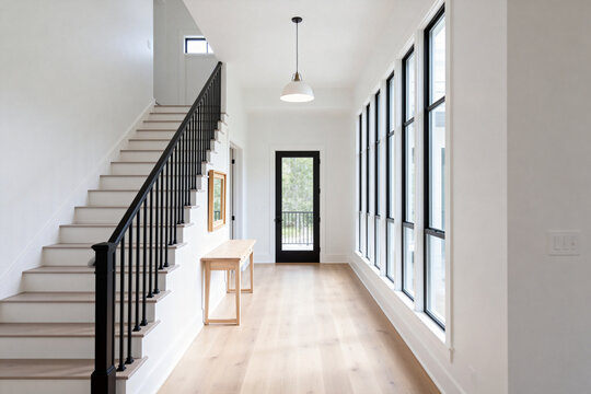Bright modern hallway with large windows, staircase, and wooden console table