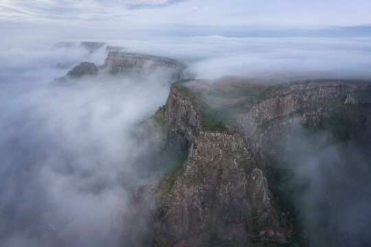 Aerial view of the Giant's Causeway cliffs shrouded in thick morning mist and fog with green plateaus and basalt rock formations in Bushmills, Northern Ireland, United Kingdom.