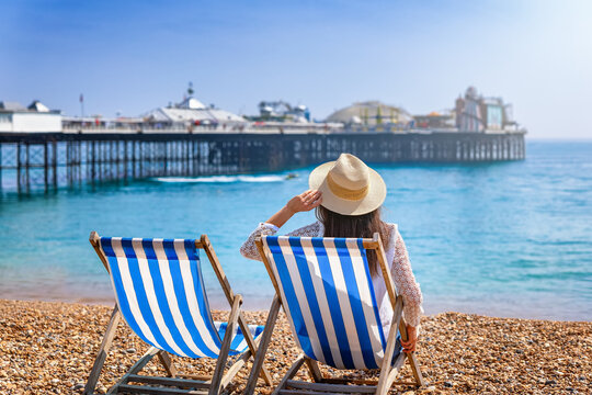 A tourist woman sits in a deckchair at the beach of Brighton, England, and looks at the famous pier